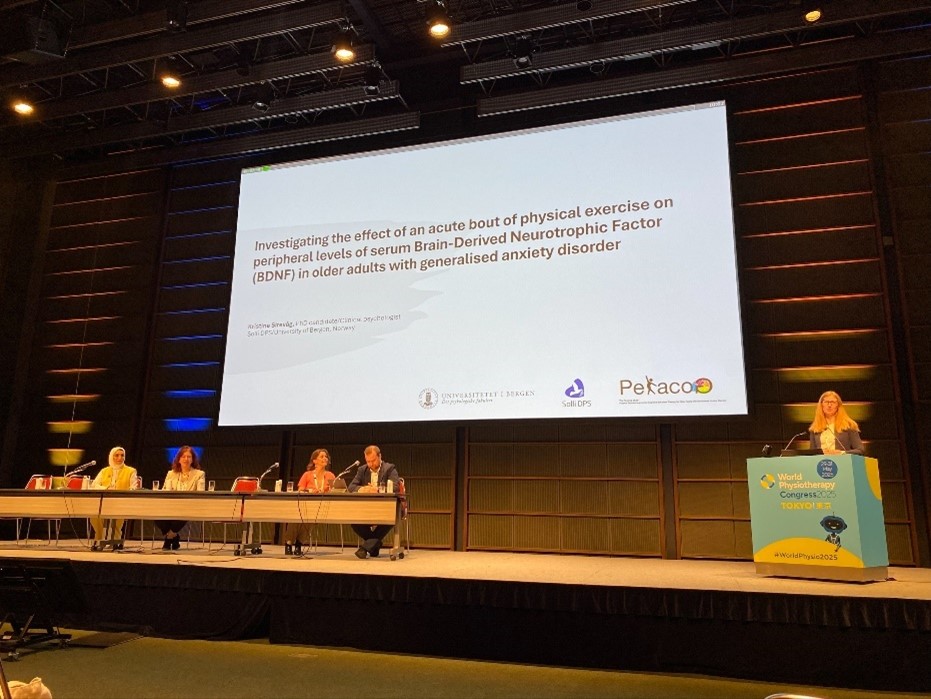 En gruppe mennesker som sitter ved et bord med en stor skjerm bak seg