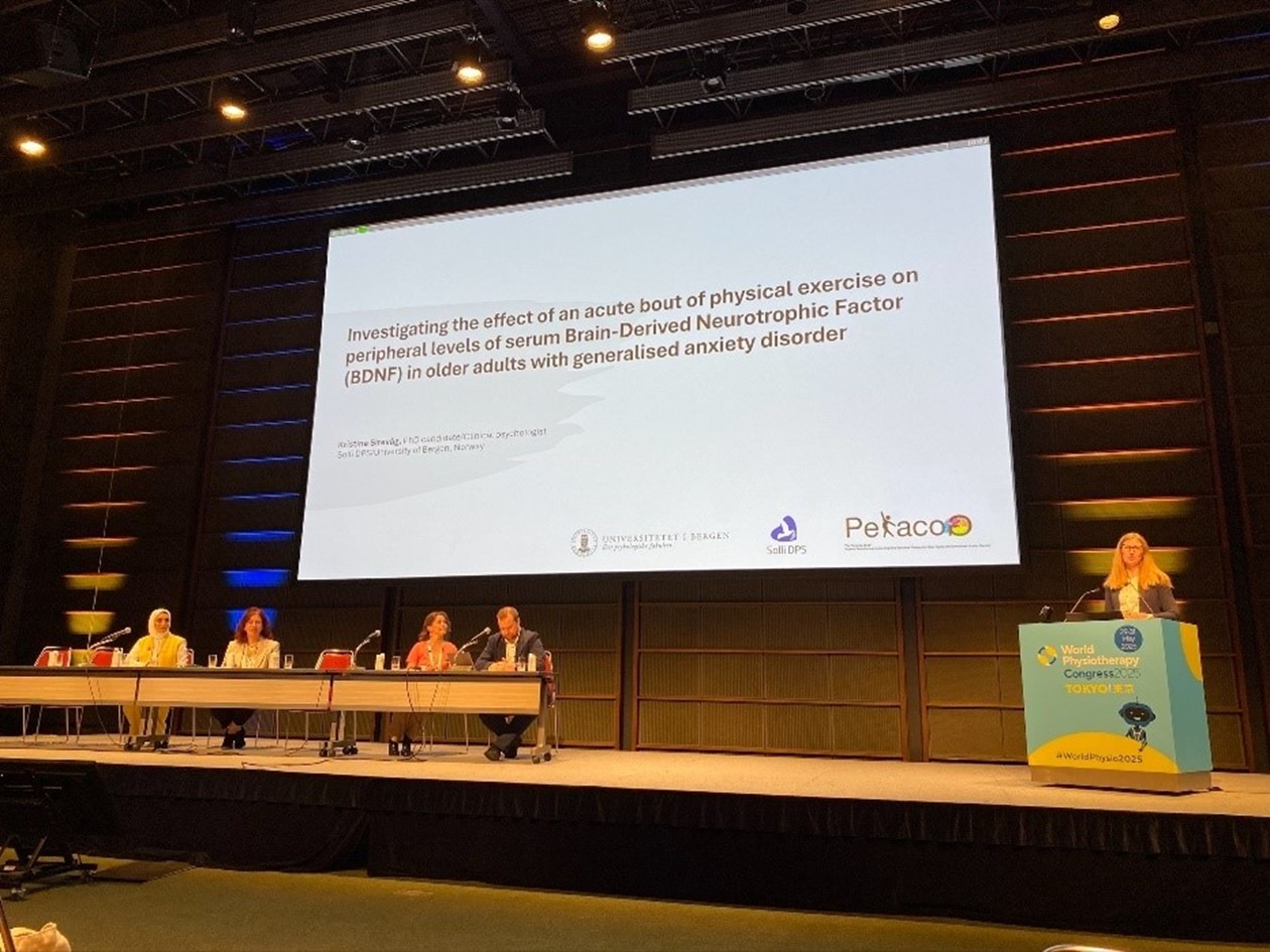 En gruppe mennesker som sitter ved et bord med en stor skjerm bak seg