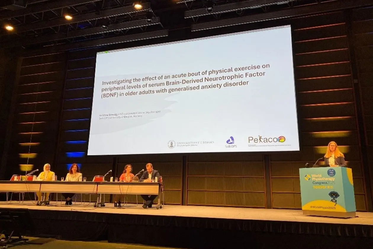 En gruppe mennesker som sitter ved et bord med en stor skjerm bak seg